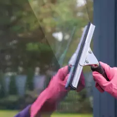 Ręce w różowych rękawiczkach myją okno ściągaczką.
