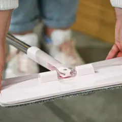 Dłonie trzymające różowy mop płaski z szarym wkładem z mikrofibry.