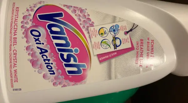 Butelka płynu Vanish Oxi Action Crystal White z etykietą i zawieszką informującą o działaniu.